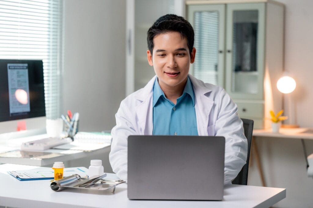 Asian doctor using laptop, providing online healthcare services in modern clinic