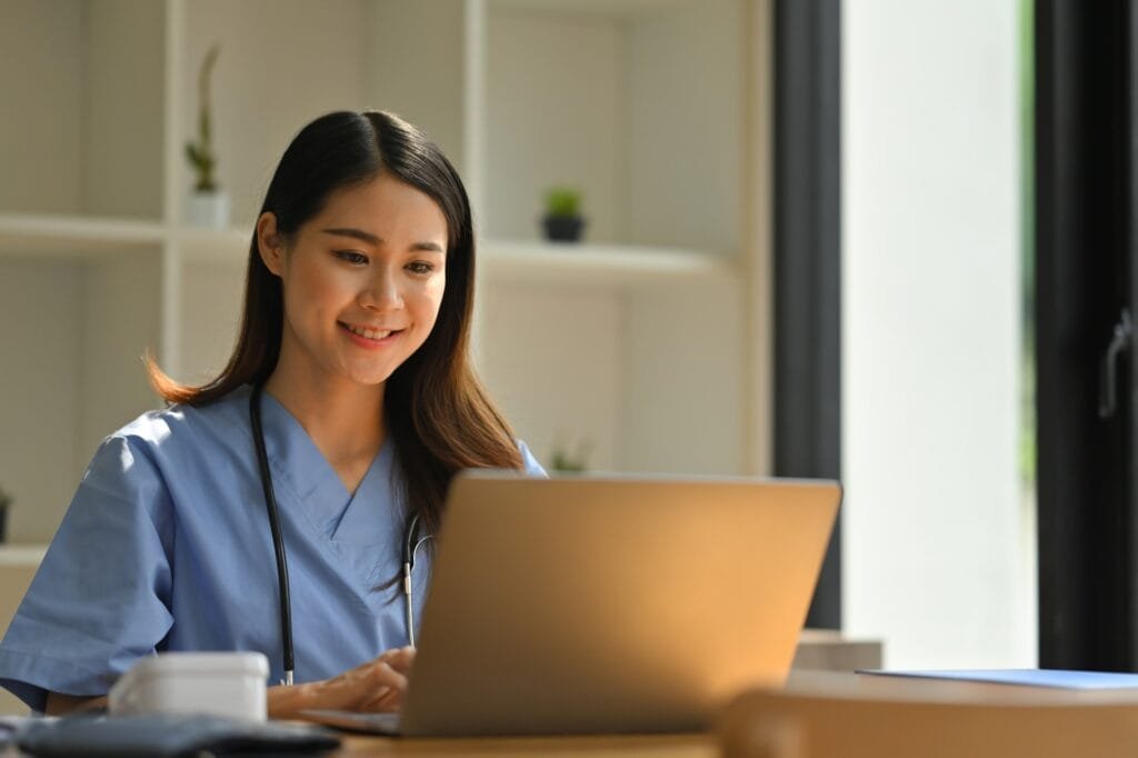 Smiling female doctor reading electronic medical records on laptop compute