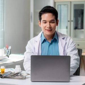 Asian doctor using laptop, providing online healthcare services in modern clinic