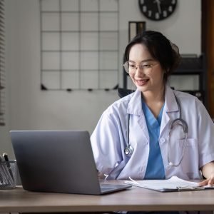 Beautiful female doctor checking patient information working with laptop on desk in doctor's office