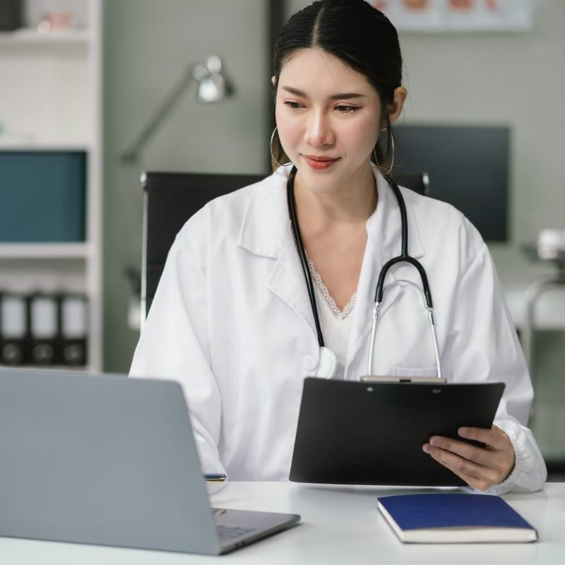 Doctor working on laptop computer and tablet and medical stethoscope on clipboard on desk