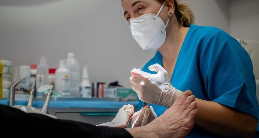 Female podiatrist in a medical mask and gloves treating the feet of a client