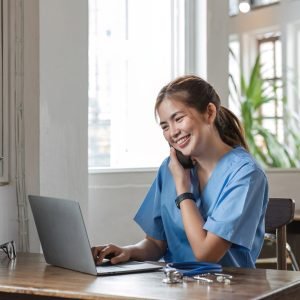 happy-female-doctor-using-laptop-to-do-data-work-and-chat-with-patients-on-the-phone-in-office-in