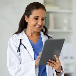 Happy middle aged lady doctor working on digital tablet
