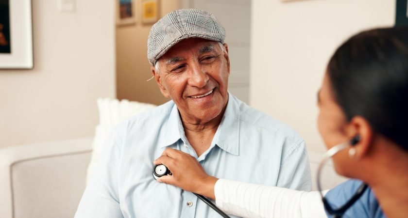 Smile, senior man and nurse with stethoscope on couch for cardiology and medical exam. Heart health