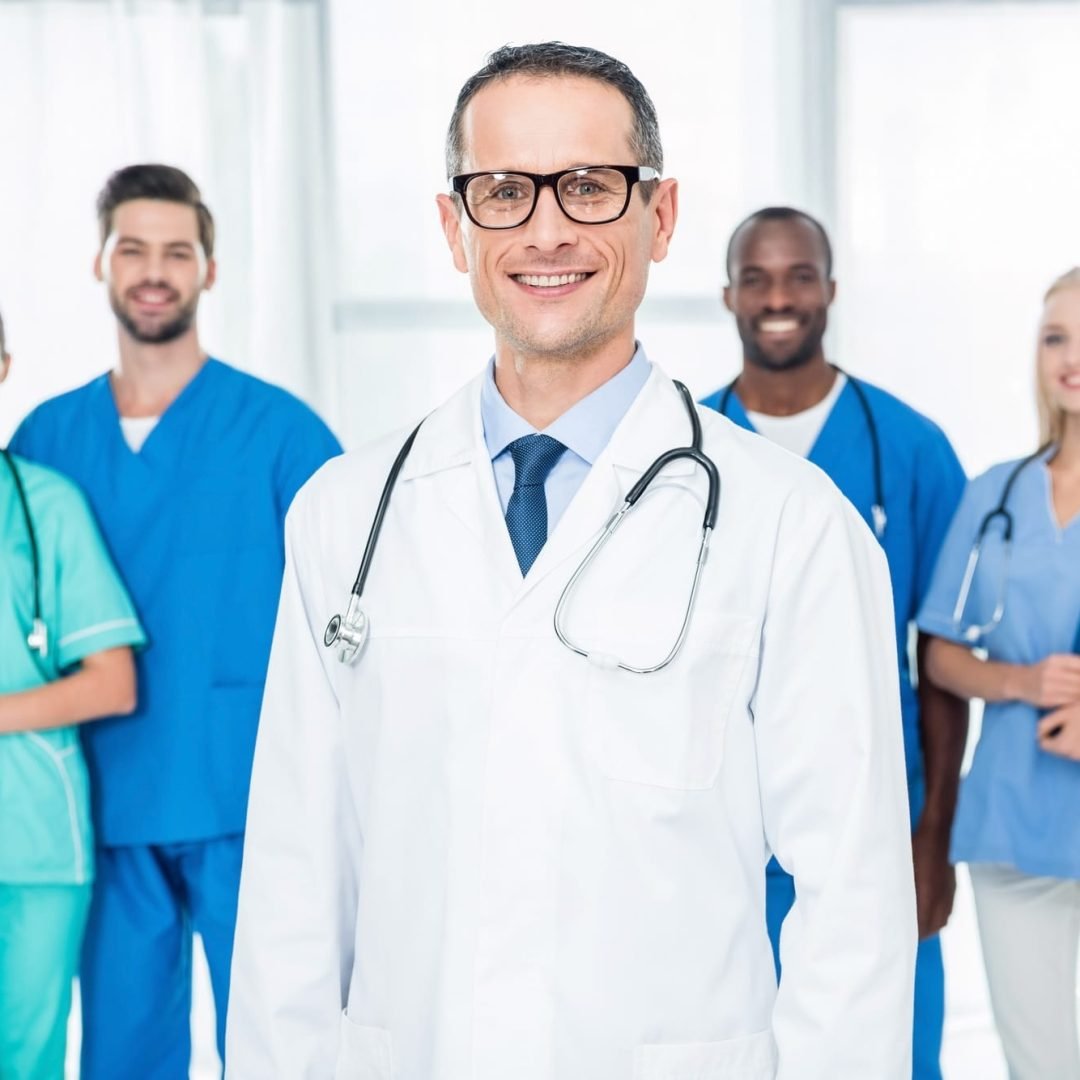 smiling mature doctor with colleagues standing together on background